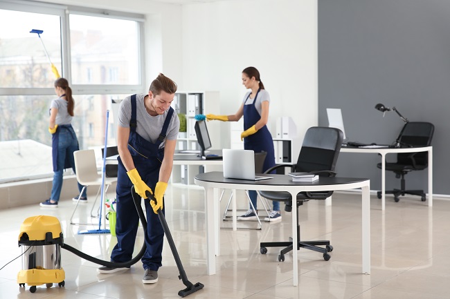 Office cleaning staff disinfecting shared workstations and vacuuming flooring inside a busy Southwest Florida office during scheduled cleaning hours